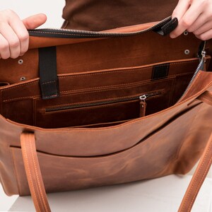 Puede incluir: Un bolso tote de cuero color canela con apertura superior, que presenta un cierre de cremallera negro, dos correas delgadas para el hombro y un compartimento interior con un bolsillo con cremallera. Incluye bandas el&aacute;sticas negras.