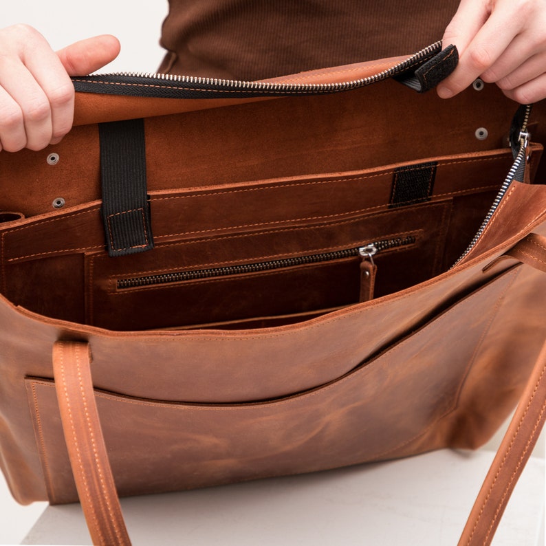 Puede incluir: Un bolso tote de cuero color canela con apertura superior, que presenta un cierre de cremallera negro, dos correas delgadas para el hombro y un compartimento interior con un bolsillo con cremallera. Incluye bandas el&aacute;sticas negras.