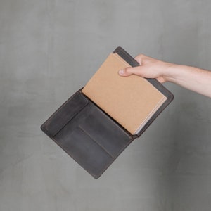 May include: A brown leather notebook cover with a brown notebook inside. The cover has a flap that closes with a snap.