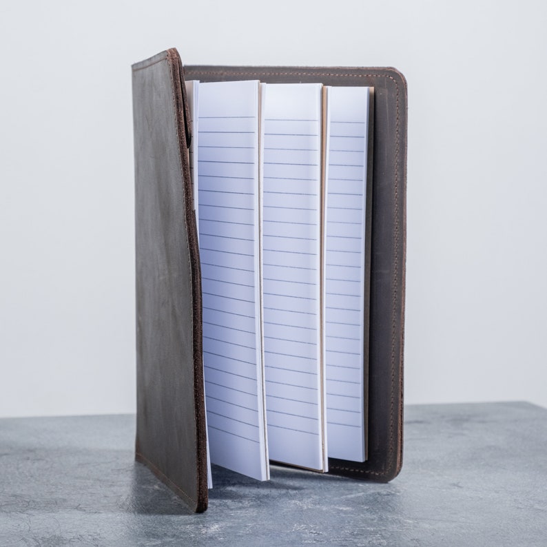 May include: A brown leather notebook with a lined paper insert. The notebook is closed and the cover is visible.