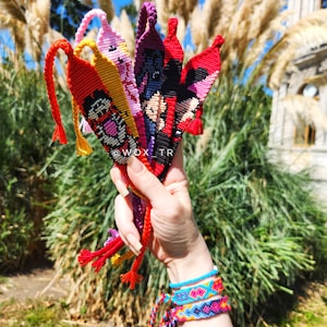 Könnte beinhalten: Eine Sammlung bunter Freundschaftsbänder mit verschiedenen Mustern und Designs. Die Armbänder sind aus buntem Stickgarn gefertigt und in verschiedenen Farben gehalten, darunter Rot, Gelb, Pink, Lila und Schwarz. Die Armbänder sind zusammengebunden und werden in einer Hand gehalten.