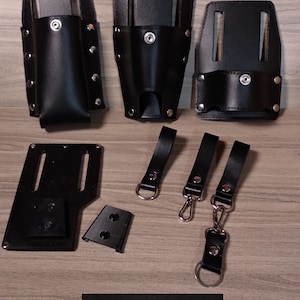May include: A set of black leather tool holders with metal rivets and a silver buckle. The holders are designed to hold tools such as screwdrivers, pliers, and hammers. The set also includes three black leather straps with silver buckles.