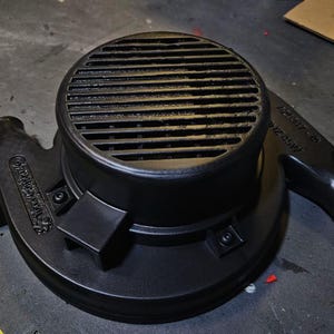 Op de afbeelding: Zwarte elektrische ventilator met een rooster en een ronde behuizing. De ventilator heeft een zwarte kunststof behuizing en een zwarte kunststof handgreep. De ventilator is gelabeld "Motor 24V 45W".