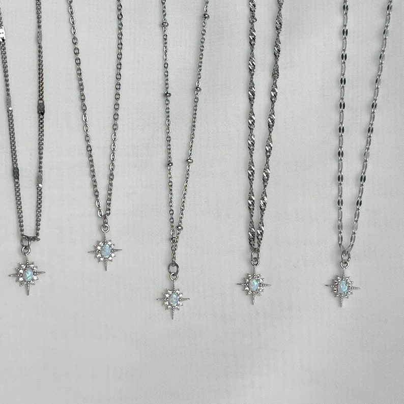 May include: Five silver necklaces with starburst pendants featuring a white opal-like stone. Each necklace has a different chain style.