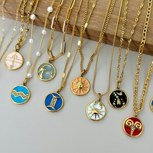 K&ouml;nnte beinhalten: Eine Sammlung goldfarbener Halsketten mit verschiedenen Anh&auml;ngerdesigns. Die Anh&auml;nger zeigen Tierkreiszeichen in Farben wie Blau, Rosa und Orange. Einige Halsketten haben Perlenakzente, andere Kettenglieder oder zarte Ketten.