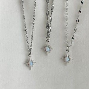 May include: Three silver necklaces with starburst pendants featuring an opal stone. Each necklace has a different chain style.