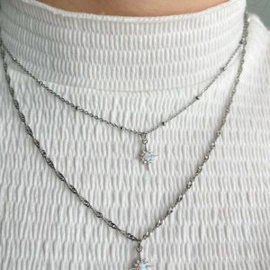 May include: Two silver necklaces with opal starburst pendants. The necklaces are layered on a white shirt.