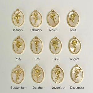 May include: Twelve oval pendants featuring gold-toned metal flower reliefs set against a white mother-of-pearl background. Each pendant is labeled with a month from January to December, representing birth flowers in a grid arrangement.