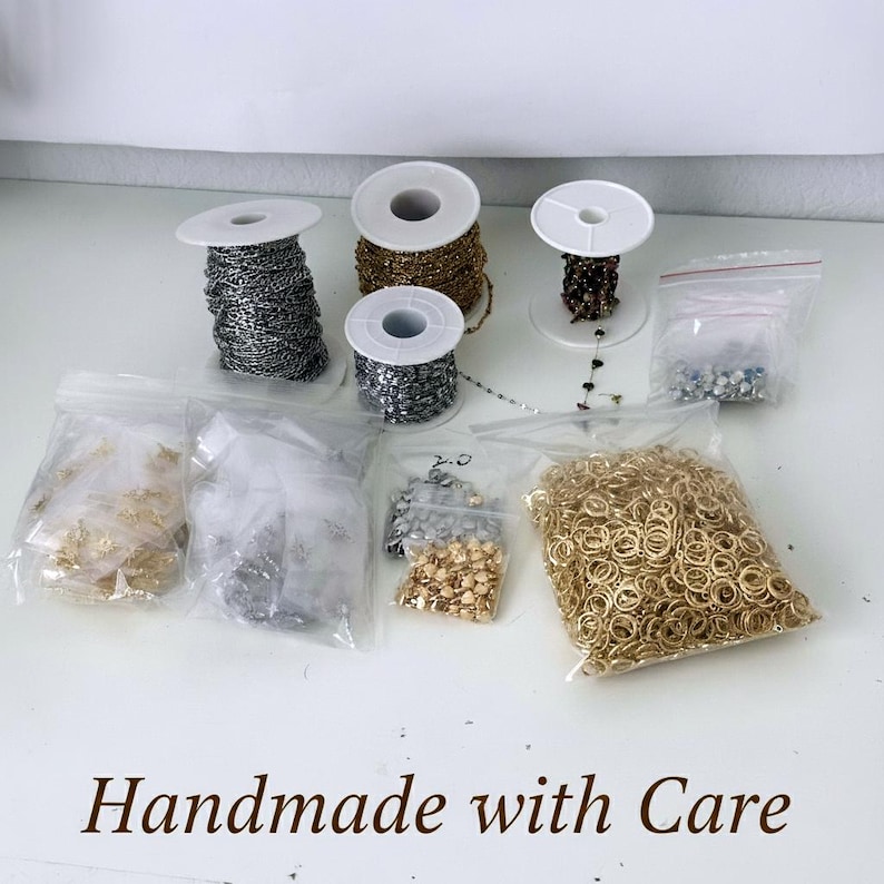 May include: A collection of jewelry making supplies including three spools of metal chain in silver, gold, and dark tones, several clear plastic bags filled with gold and silver jump rings, small metal charms, and beads. The text Handmade with Care is visible.