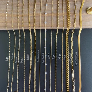 K&ouml;nnte beinhalten: Eine Auswahl goldfarbener Halsketten mit verschiedenen Kettenstilen, darunter Lip, Flat Curb, Beaded, Twist, Figaro, Curb, Thin Herringbone, Pearl Beaded, Dainty, Rope, Vine, Cuban, Link (Paperclip) und Herringbone.
