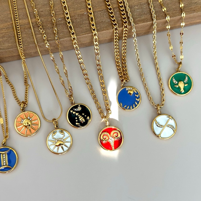 K&ouml;nnte beinhalten: Goldfarbene Halsketten mit verschiedenen Sternzeichen-Anh&auml;ngern. Jeder Anh&auml;nger hat einen andersfarbigen Emaille-Hintergrund und ein detailliertes Sternzeichen-Symbol. Die Ketten variieren im Stil, darunter Panzer-, Seil- und Kabelketten. Die Anh&auml;nger sind rund und haben einen goldenen Rand.