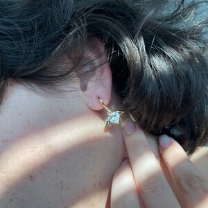 Może przedstawiać: Złote kolczyki koła z wiszącym sercem z kryształu i małymi skrzydłami.