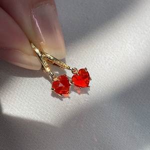 May include: A pair of gold hoop earrings with dangling red heart-shaped charms.