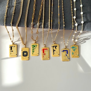 May include: Seven gold-toned necklaces featuring rectangular pendants with colorful enamel designs. The pendants depict various motifs including playing card figures, an eye, a snake, a sun, a moon, and floral patterns, suspended from diverse gold chains.