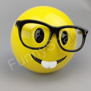 Puede incluir: Una figurita de cara sonriente amarilla con una sonrisa de dientes y gafas de montura negra.