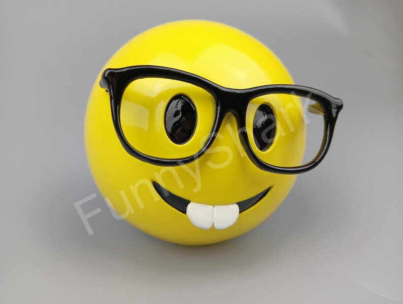Puede incluir: Una figurita de cara sonriente amarilla con una sonrisa de dientes y gafas de montura negra.