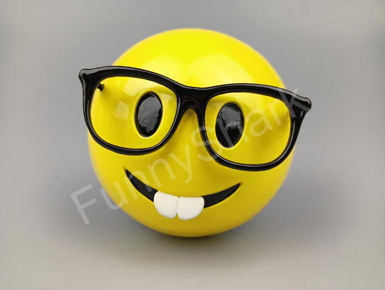 Puede incluir: Hucha amarilla con cara sonriente, gafas de pasta negra y una amplia sonrisa.