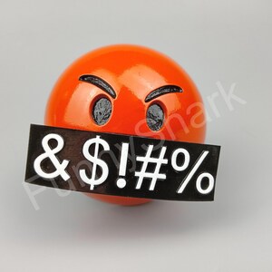 May include: A bright orange sphere with black eyes and eyebrows, and a black rectangle covering the mouth. The rectangle displays the symbols & $ ! # % in white. The design is a humorous, expressive representation.