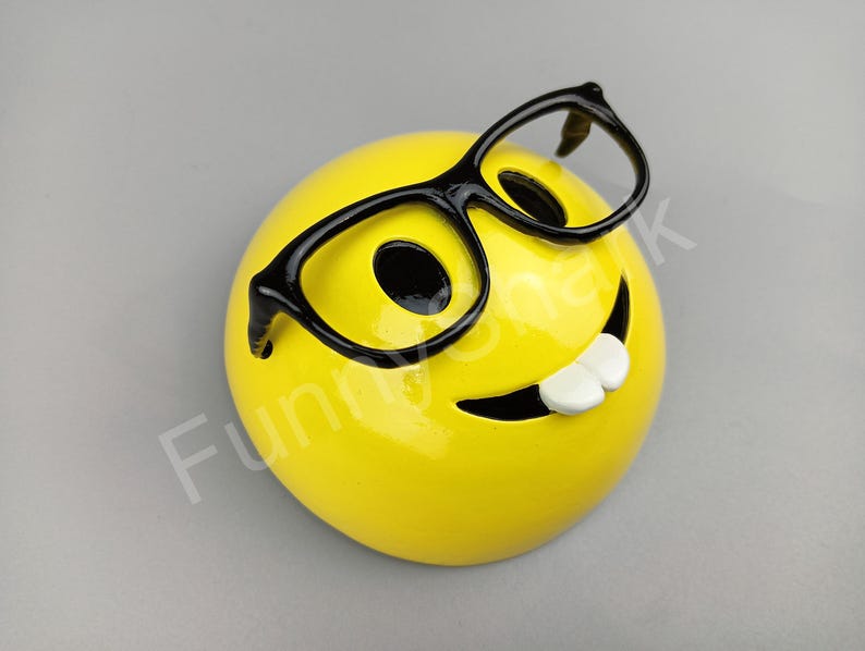 Puede incluir: Cara sonriente de cer&aacute;mica amarilla con gafas de montura negra y una amplia sonrisa.