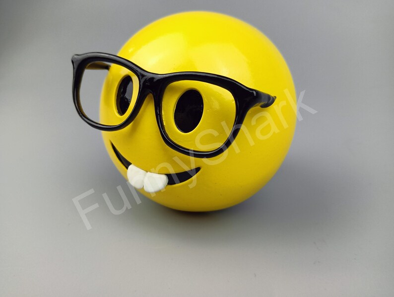 Puede incluir: Una cara sonriente amarilla con una sonrisa de dientes y gafas de montura negra.