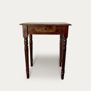 May include: A small, antique wooden table with a single drawer and turned legs. The table is a rich, dark brown colour, and the drawer has a small, round knob. The table's dimensions are approximately 76 cm tall, 61 cm wide, and 46 cm deep.