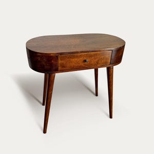 May include: A mid-century modern oval-shaped side table with a single drawer. The table is made of dark brown wood and has four tapered legs. The drawer has a small, round, dark knob. The table is approximately 30 inches long, 18 inches wide, and 24 inches tall.