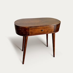May include: A mid-century modern oval-shaped side table with a single drawer. The table is made of dark brown wood and has four tapered legs. The drawer has a small, round, dark knob.