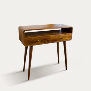 Könnte beinhalten: Konsole aus Holz im Mid-Century-Modern-Stil mit zwei Schubladen und einem Regal. Der Tisch hat eine warme braune Oberfläche, abgerundete Kanten und konische Beine. Die Schubladen haben kleine, runde Knöpfe.