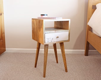 May include: A wooden bedside table with a white drawer and a shelf. The table has four tapered legs and a light wood finish.