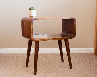May include: A mid-century modern style wooden end table with a curved open shelf and four tapered legs. The table is made of dark wood and has a natural wood finish.