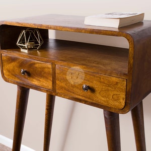 May include: A wooden side table with two drawers and a shelf. The table has a curved top and tapered legs. The table is made of dark wood and has a natural finish.
