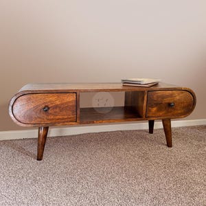 May include: A dark brown wooden coffee table with a curved front and two drawers. The table has a shelf and sits on four tapered legs.