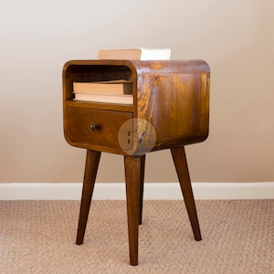 May include: A dark brown wooden bedside table with a curved front and a single drawer. The table has four legs and a shelf above the drawer. There are books on the shelf.