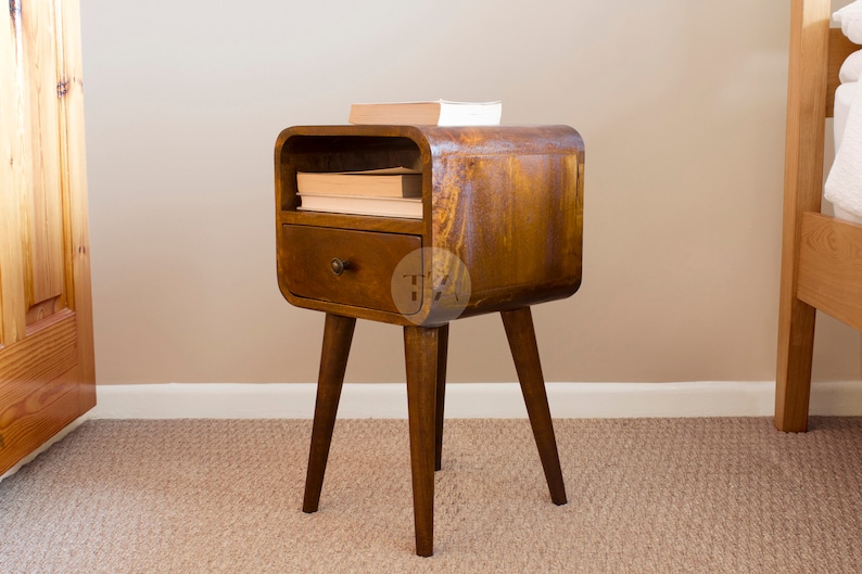 May include: A dark brown wooden bedside table with a curved front and a single drawer. The table has four legs and a shelf above the drawer. There are books on the shelf.