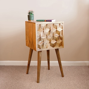 May include: A wooden nightstand with a geometric design on the drawer front. The nightstand has four tapered legs and is sitting on a beige carpet.