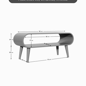 Op de afbeelding: Een grijze houten salontafel met een gebogen bovenblad en een open plank. De tafel is 75 cm breed, 30 cm diep en 20 cm hoog. De plank is 86 cm breed en 17 cm diep.