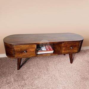 May include: A dark brown wooden coffee table with a curved top and two drawers. The table has a shelf underneath and is supported by four tapered legs.