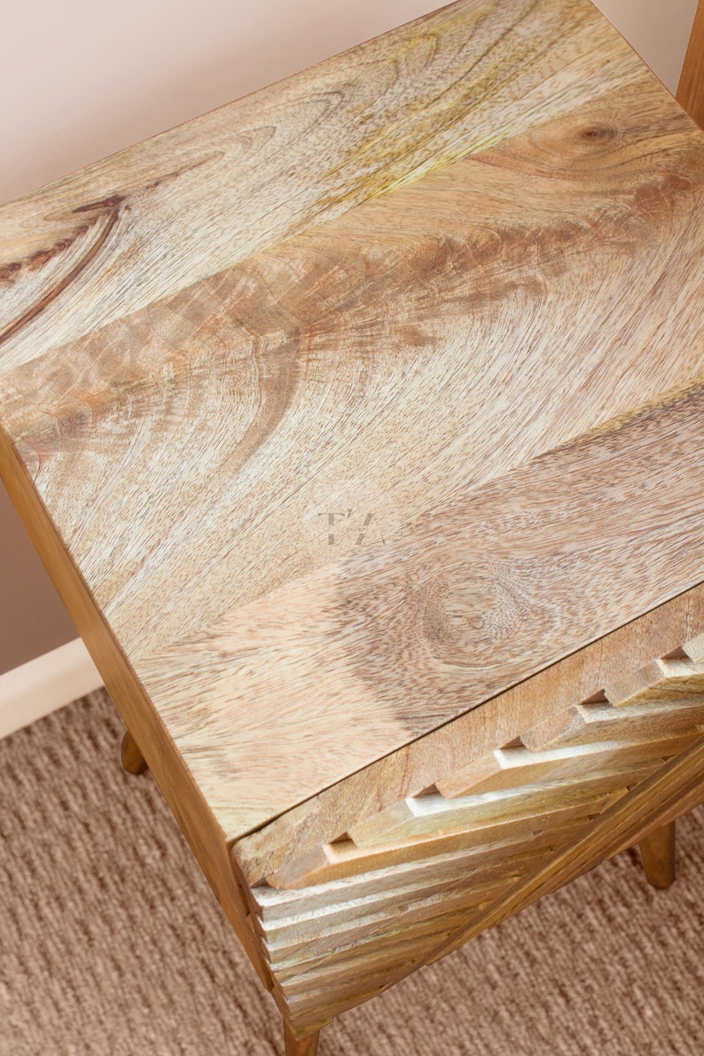 May include: A wooden side table with a unique geometric design on the front. The top of the table is made of light wood with a natural grain pattern.
