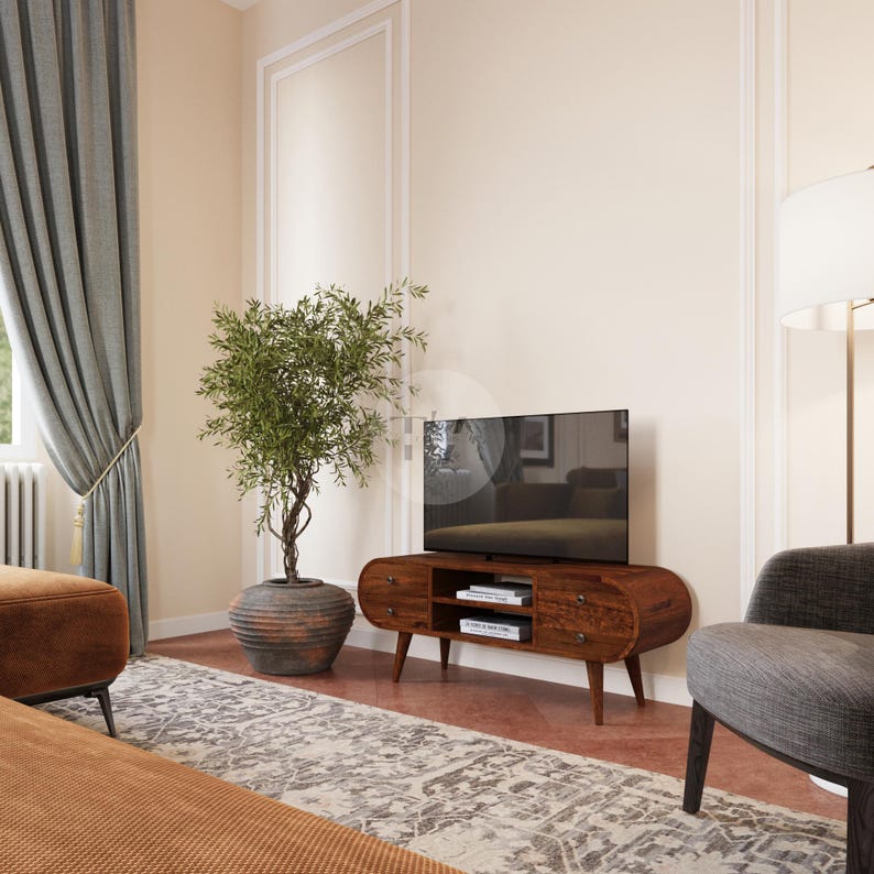 May include: A dark wood oval-shaped TV stand with three drawers and two shelves. The stand has a modern design with tapered legs. A flat screen TV is mounted on the stand. A potted olive tree and a gray armchair are in the background.