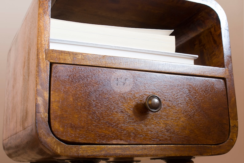 May include: A wooden nightstand with a curved top shelf and a drawer with a metal knob. The shelf has a stack of books on it.
