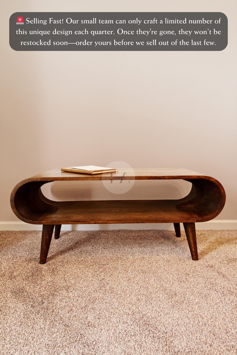 Op de afbeelding: Een donkerbruine houten salontafel met een gebogen bovenblad en een lager plankje. De tafel heeft vier poten en staat op een beigekleurig tapijt.