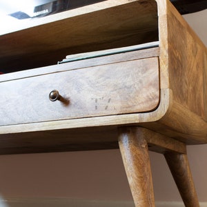 May include: A wooden TV stand with a drawer and a shelf. The stand has a curved design and four legs.