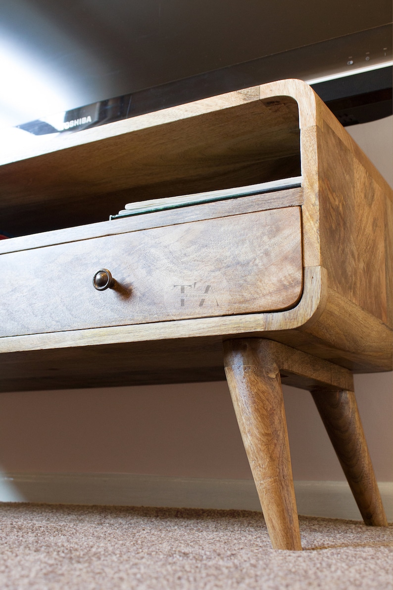 May include: A wooden TV stand with a drawer and a shelf. The stand has a curved design and four legs.