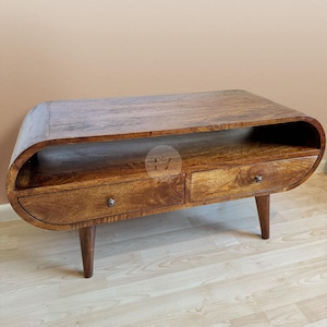 Op de afbeelding: Een houten salontafel met een gebogen bovenblad en twee laden. De tafel heeft een donkerbruine afwerking en wordt ondersteund door vier poten.
