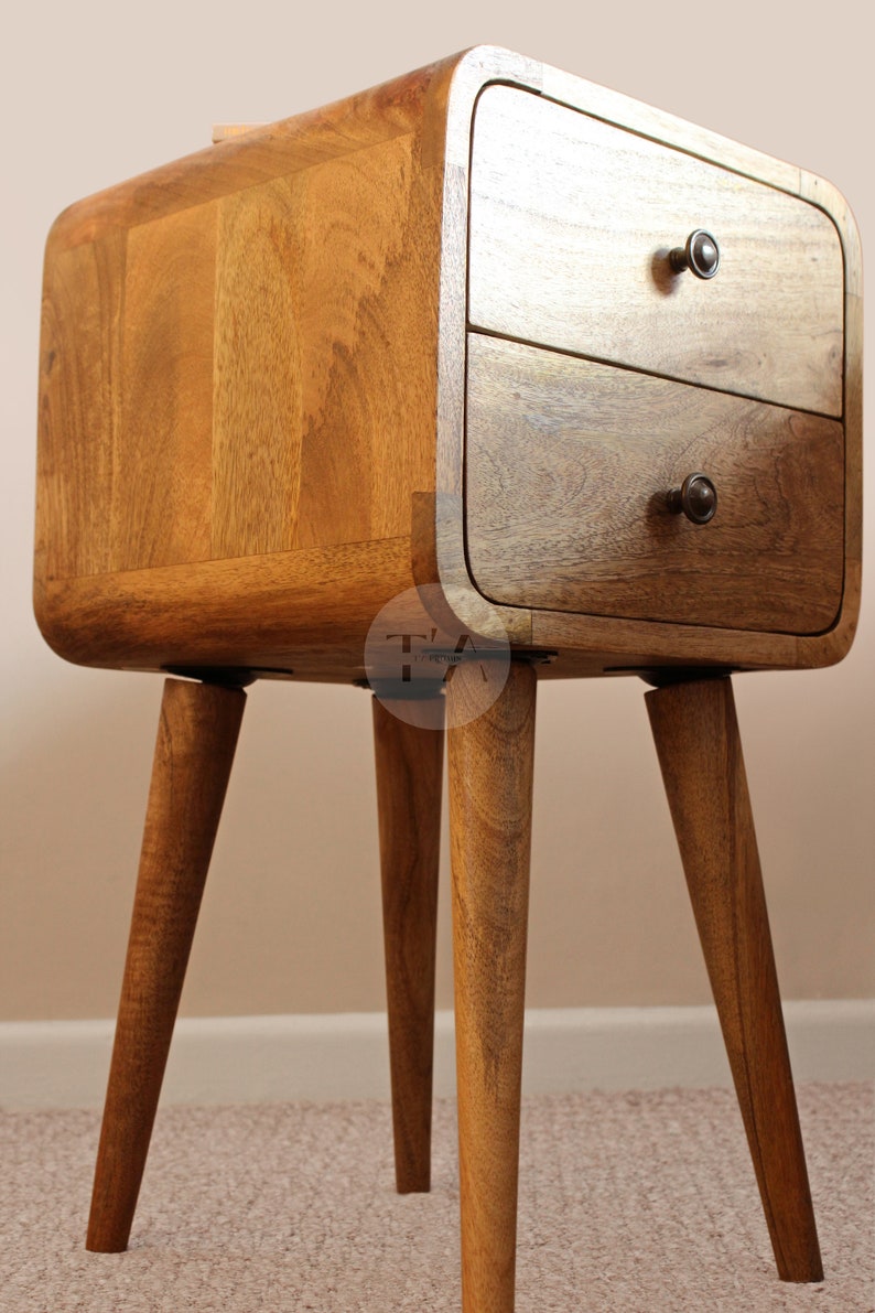 May include: A wooden bedside table with two drawers and rounded edges. The table has four tapered legs and is made of a light brown wood.