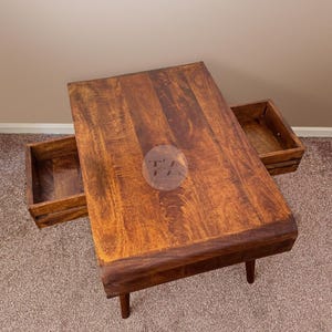 May include: A wooden coffee table with two drawers. The table has a dark brown finish and a curved edge. The drawers are open and reveal a light brown interior.