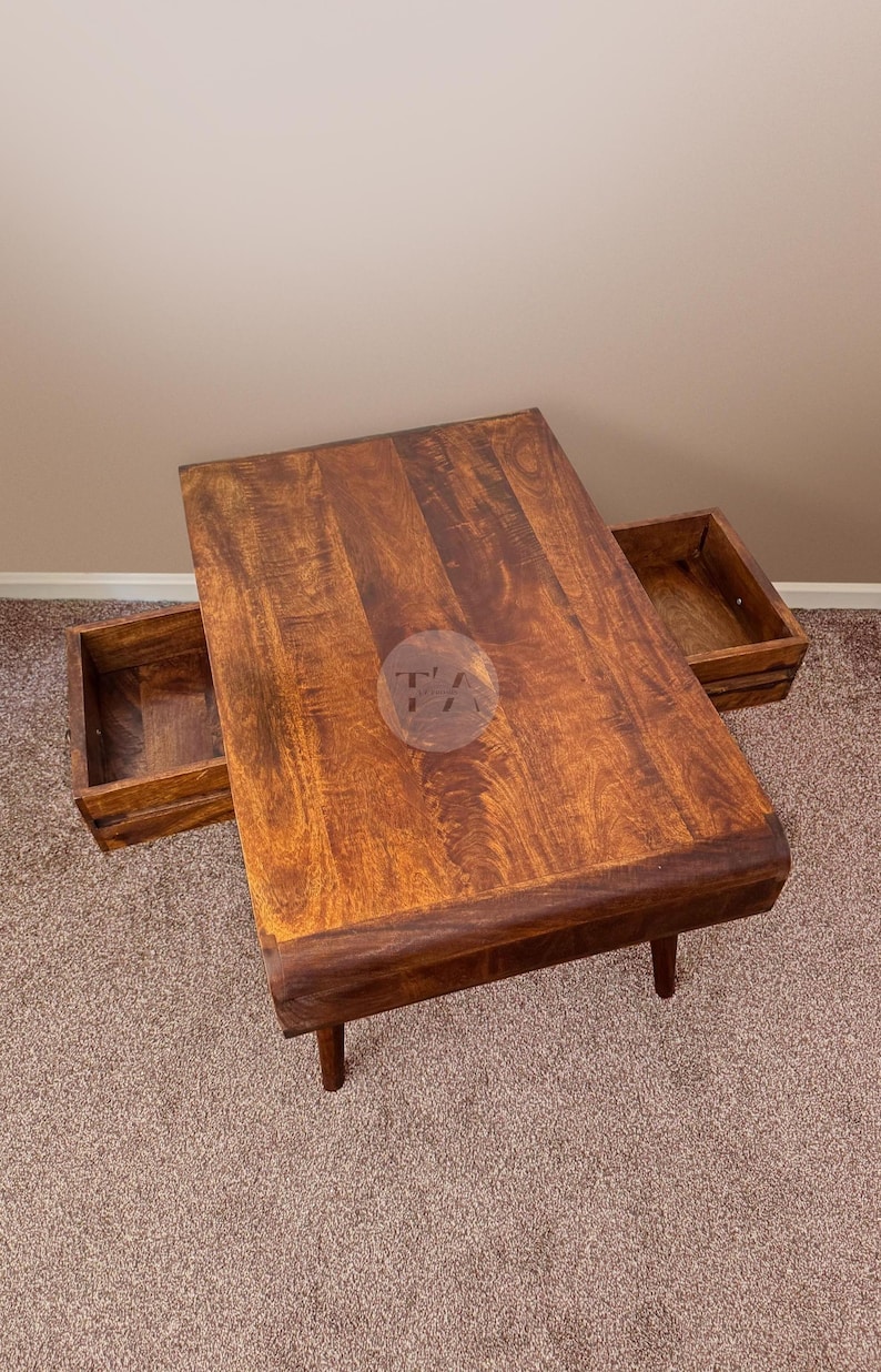 May include: A wooden coffee table with two drawers. The table has a dark brown finish and a curved edge. The drawers are open and reveal a light brown interior.