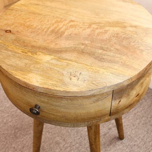 May include: A round wooden side table with a single drawer and tapered legs. The table is made of light wood and has a natural finish.