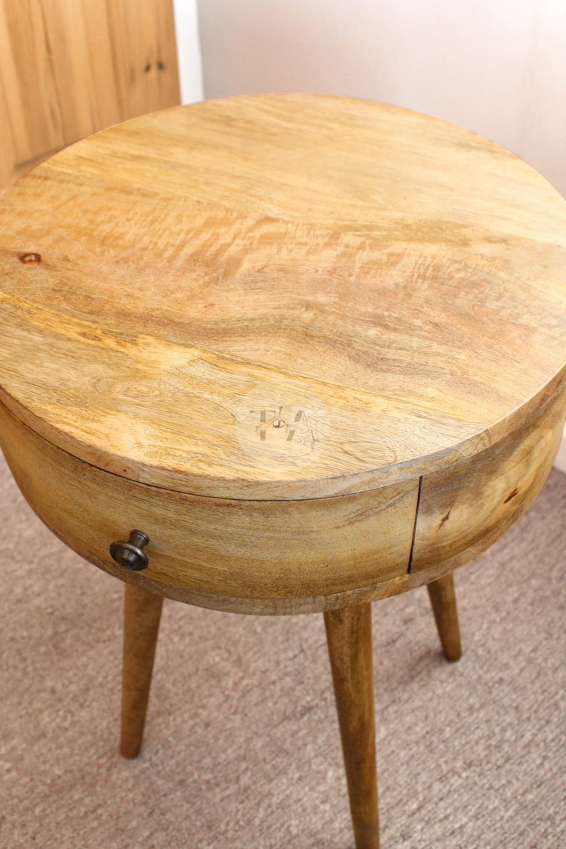 May include: A round wooden side table with a single drawer and tapered legs. The table is made of light wood and has a natural finish.