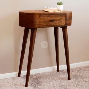 May include: A dark brown wooden side table with a single drawer and four tapered legs. The table has a rounded top and a slightly oval shape.